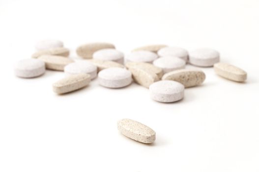 Selective focus on single multi-vitamin in the foreground with many vitamins in the background with soft focus isolated on white background