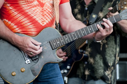 Two rock and rollers at a music festival with selective focus on the forground hands strumming the guitar