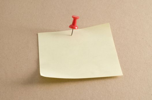 Macro of a pushpin holding a sticky note on a kraft folder