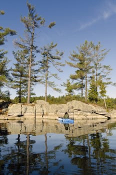Kayaker checks the Canadian Shield rock formation on a calm tranquil northern lake in September