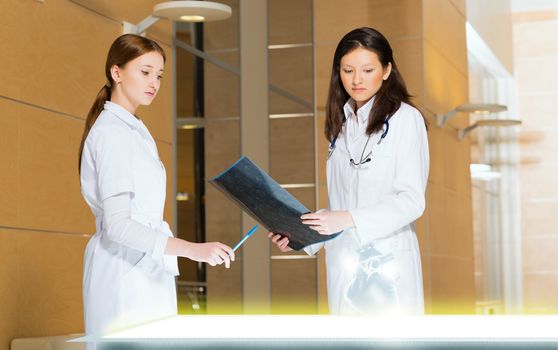 two doctors stand near glowing table discussing. projected objects on a desk