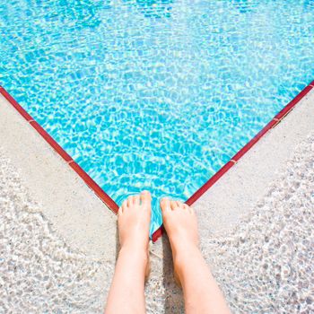 A child's feet at the edge of a bright blue swimming pool