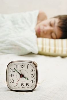 Closeup of alarm clock and sleeping boy at the background
