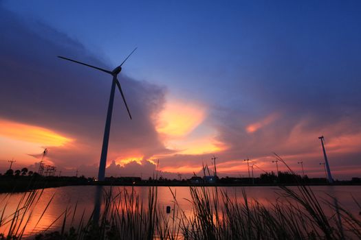 Wind turbine in the small wind power plant. Located next to a large lake. Sun in the sun to set. There is a beautiful color light in the sky is background.