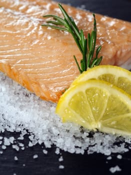 Photo of a cooked salmon steak with rosemary and lemon slices on a bed of sea salt.