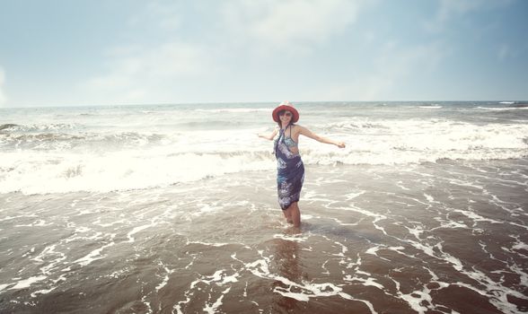 Happy brunette lady with hat and sunglasses standing at the beach