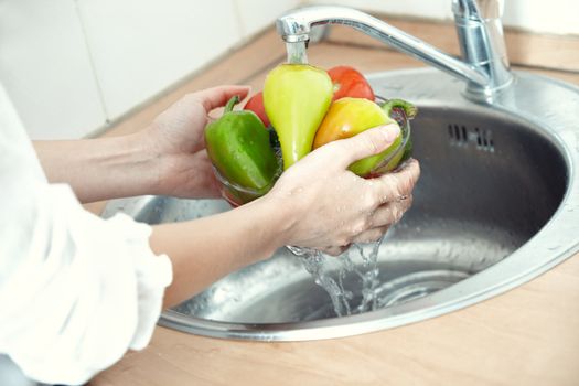 Hands of woman washing vegetables at her kitchen