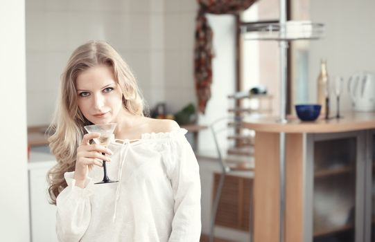 Blond lady holding wine glass with beverage at the kitchen