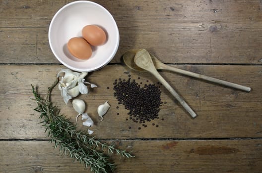 Kitchen ingredients comprising of brown eggs in a white bowl, garlic, fresh rosemary and black lentils with two wooden spoons. All set on a landscape format against a wooden background. Copy-space available.