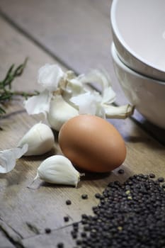 Close up detail of some kitchen ingredients comprising of a brown egg, garlic, fresh rosemary and black lentils. All set on a portrait format against a wooden background wirth copy-space available.