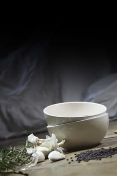 Kitchen ingredients comprising of white bowls,garlic, fresh rosemary and black lentils. All set on a portrait format against a wooden background with plenty of copy-space available above.