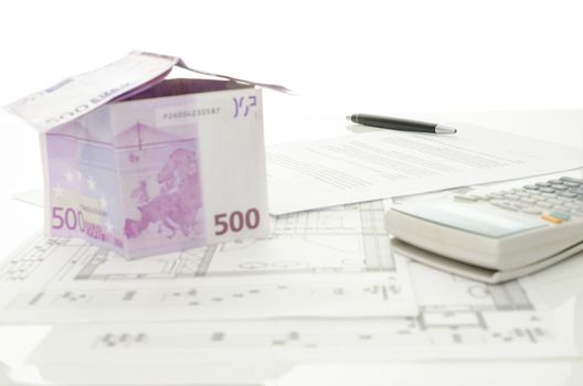 Pen over contract of house sale with house made of  Euro money and  architectural building plan on a white table. Focus on a pen.