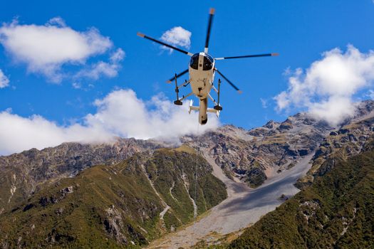 Small helicopter hovering mid-air in blue sky over mountains of Southern Alps New Zealand