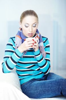 Sick woman in sweater and scarf holding cup with hot tea