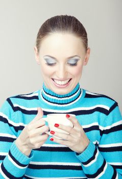 Smiling woman indoors in striped sweater holding cup with tea or coffee