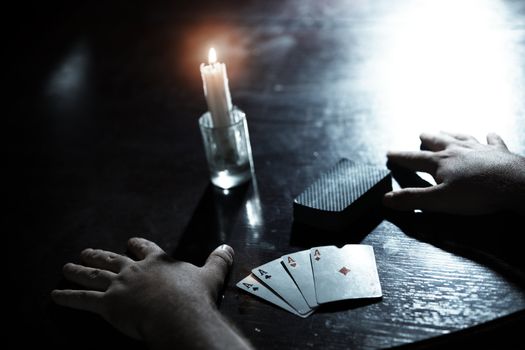 Human hands on a dark table with pack of cards and flaming candle