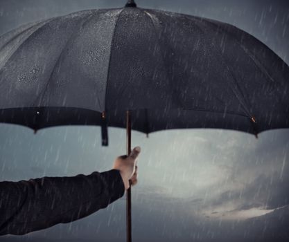 Human hands holding big black umbrella under the heavy rain