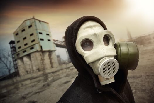Man in protective gas mask near the industrial plant during radioactive sunset. Artistic colors and grain added