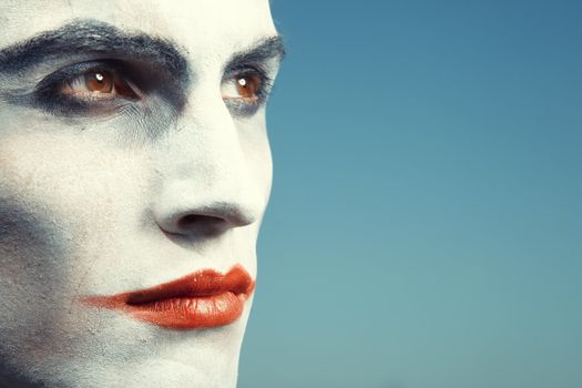 Sad clown with makeup on a blue background