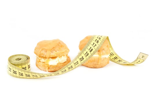concept of slimming, caramel cakes with measuring tape on white background