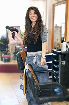Happy hairdresser holding hairdryer in hair salon