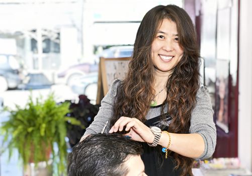 Happy hairdresser cutting hair in her salon