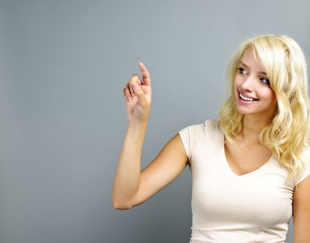 Smiling blonde caucasian woman pointing to the side on grey background
