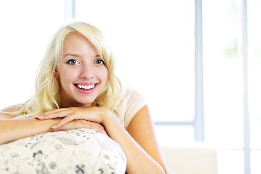 Portrait of smiling blonde woman relaxing on couch in living room at home