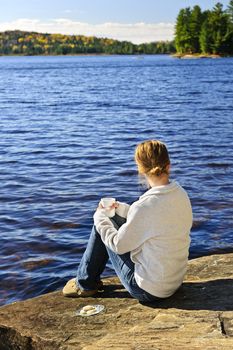 Young woman sitting and relaxing on lake shore in Algonquin Park, Canada