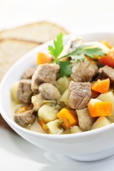 Bowl of hearty beef stew with vegetables served with rye bread