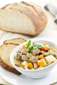 Bowl of hearty beef stew with vegetables served with rye bread