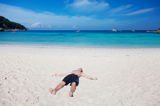 man lies on a  beach on an ocean coast