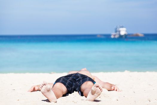 man lies on a  beach on an ocean coast