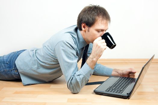 young man with cup using laptop  lying on the floor in the room