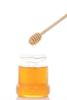 Pot of honey and wooden stick are on a table.