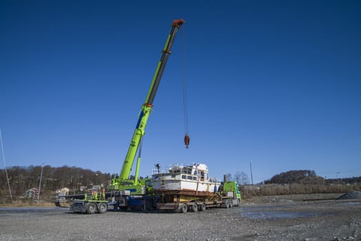 The boat was transported by trailer and was unloaded with a huge mobile crane on the quay at the port of Halden, Norway. The picture is shot one day in March.