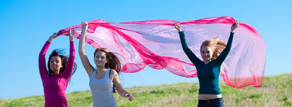 three young beautiful woman jumping with tissue into the field against the sky
