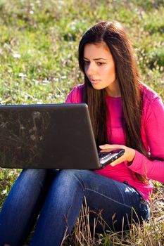 young beautiful woman with a laptop sitting in the field on sky background 