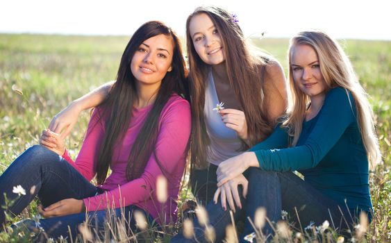 three young beautiful woman sitting in a field on the  sky background 