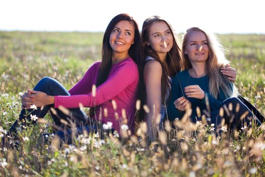 three young beautiful woman sitting in a field on the  sky background 