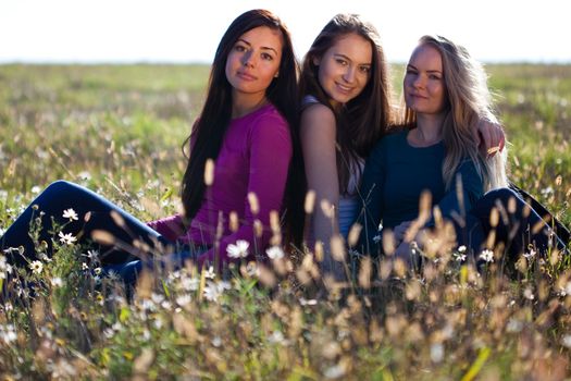 three young beautiful woman sitting in a field on the  sky background 