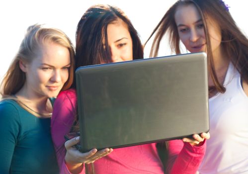 three young beautiful woman with a laptop in the field on sky background 