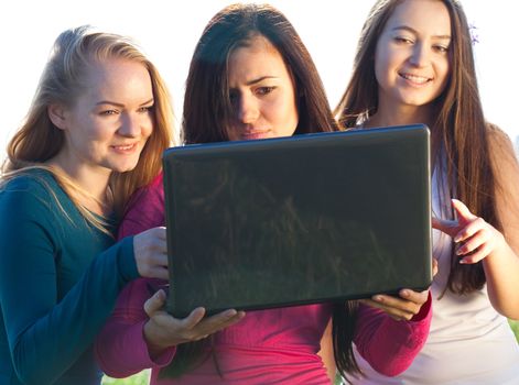 three young beautiful woman with a laptop in the field on sky background 