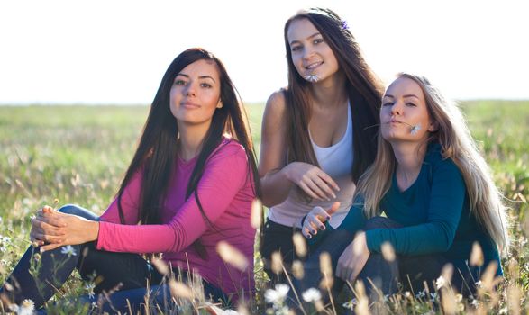 three young beautiful woman sitting in a field on the  sky background 