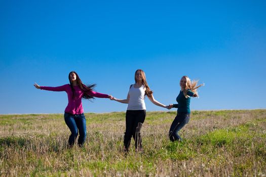 three young beautiful woman jumping into the field against the sky