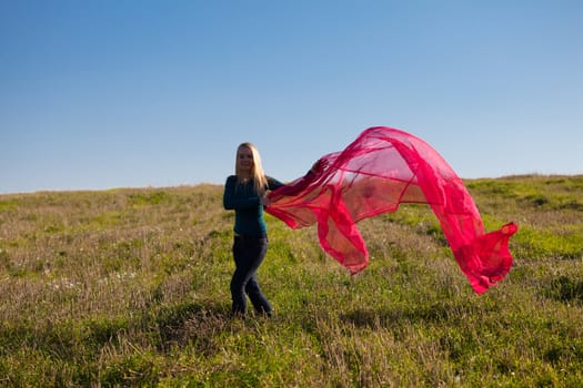 young beautiful woman jumping with tissue into the field against the sky