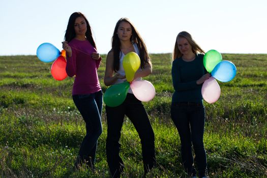 three young beautiful woman with balloons into the field against the sky