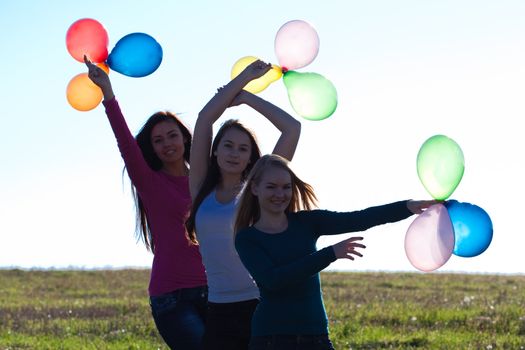 three young beautiful woman with balloons into the field against the sky