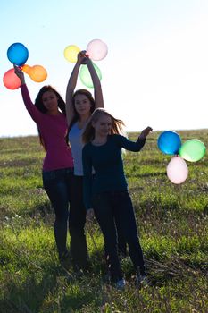 three young beautiful woman with balloons into the field against the sky