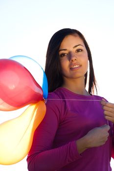 young beautiful woman with balloons into the field against the sky